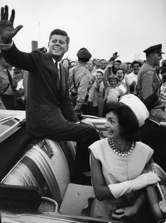 an old black and white photo of two people in a car waving to the crowd