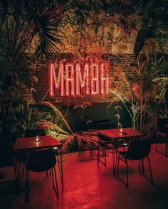 the restaurant is lit up with red lights and palm trees in front of it, which reads mamba