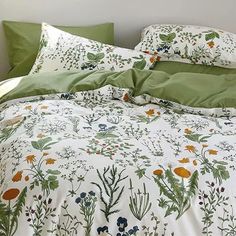 a bed covered in green and white sheets with flowers on it, next to a window