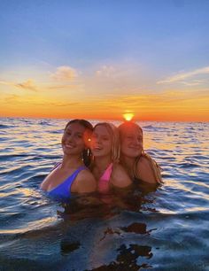 three girls are in the water at sunset