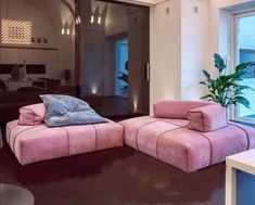 a large pink couch sitting in front of a window next to a potted plant