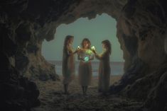 three women standing in front of a cave with lights on their hands and one holding a glowing ball