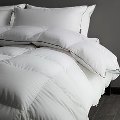 an unmade bed with white pillows and black piping on the comforter is shown