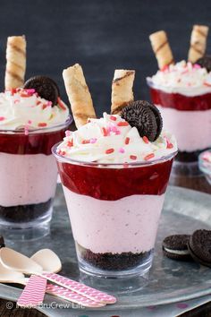 three dessert cups with oreo cookies on top and red liquid in the middle, topped with whipped cream and sprinkles