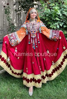 a woman in a red and gold dress standing on the grass with her arms outstretched