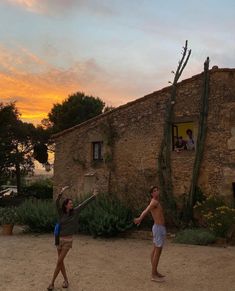 two people are playing frisbee in front of an old stone building at sunset