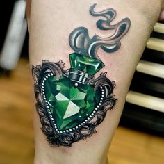 a woman's leg with a green heart shaped tattoo on her thigh and an ornate frame around it