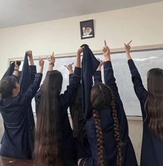 several girls in black dresses are holding their hands up above their heads as they look at the chalkboard