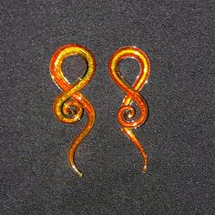 an orange and yellow pair of earrings sitting on top of a black surface