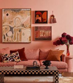 a living room with pink walls and art hanging on the wall above the couches