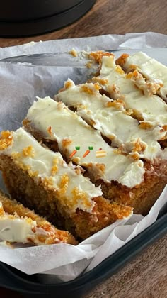 carrot cake with white frosting and sprinkles in a black container on a wooden table