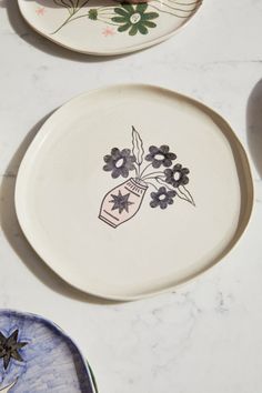 two plates with flowers painted on them sitting on a counter top next to each other