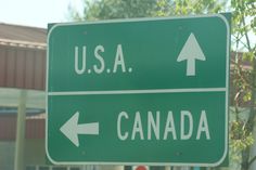 a green street sign with an arrow pointing to the us a and canada on it