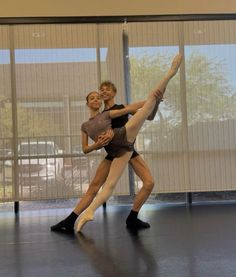 two people are doing ballet moves in front of a large window with sheer drapes