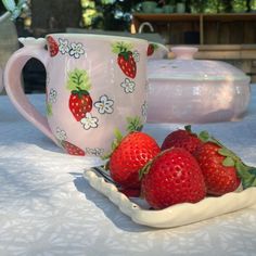 two strawberries sit on a plate next to a mug