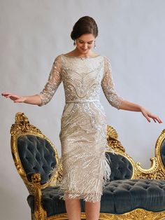 a woman standing in front of a couch wearing a dress with fringes on it