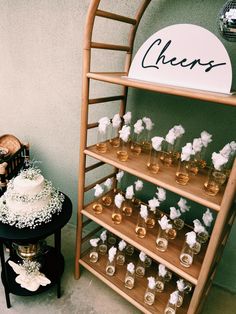 a table topped with a cake and lots of glasses filled with liquid next to a sign that says cheers