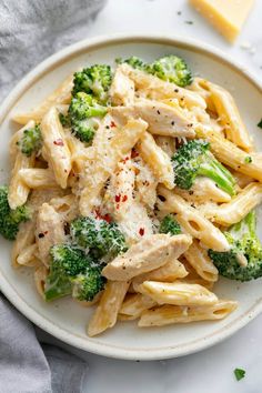 pasta with chicken and broccoli on a white plate next to cheese wedges