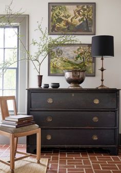 a dresser with two vases on top of it next to a lamp and paintings