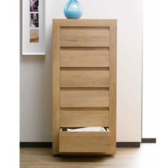 a wooden cabinet with drawers and a blue vase on it's top shelf next to a white wall