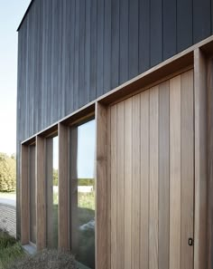 two wooden doors are open in front of a black building with windows and grass on the ground