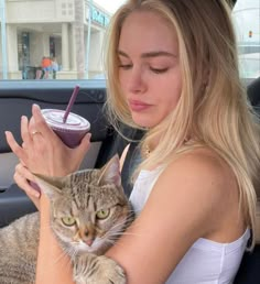 a woman holding a cat in the back seat of a car while she holds a smoothie