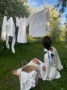 a woman sitting in the grass next to clothes hanging on a line and drying off