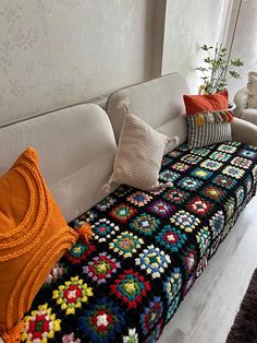 a white couch with multicolored crocheted blankets on it's back