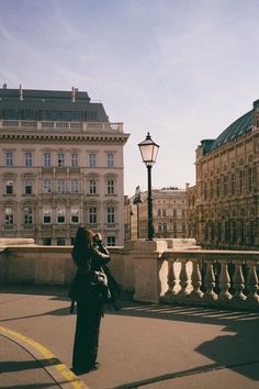 a woman is standing on a bridge looking at something in the distance with buildings behind her