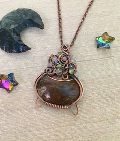 a wire wrapped necklace with a stone pendant and two other pieces of jewelry on a table