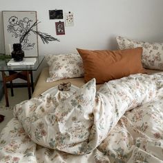 an unmade bed with many pillows and blankets on top of it, next to a small table