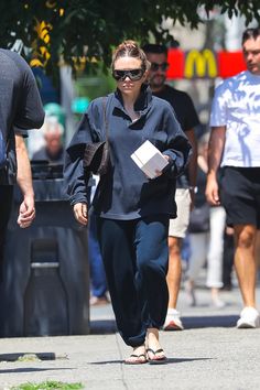 a woman walking down the street while wearing sunglasses and carrying a book in her hand