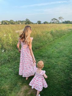 a mother and her child walking in the grass holding hands with each other on a sunny day