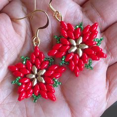 a pair of red and green flower earrings on a person's left hand,