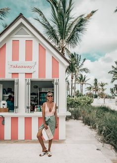 a woman standing in front of a pink and white striped kiosk on the beach