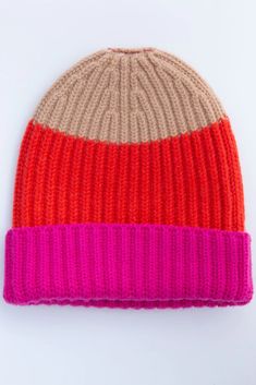 an orange and pink knitted beanie hat on a white background with the color block