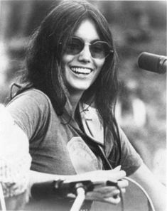 an old photo of a woman with sunglasses on holding a guitar and singing into a microphone