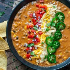 a black bowl filled with chili cheese and tortilla chips on top of a wooden table