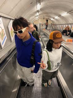 two people on an escalator pointing at something in the distance while wearing sunglasses