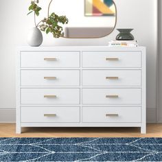 a white dresser sitting next to a mirror on top of a wooden floor