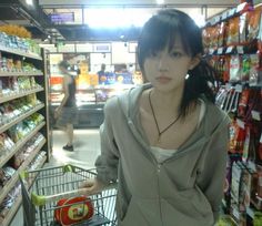 a woman standing in front of a grocery cart with food on the shelves behind her