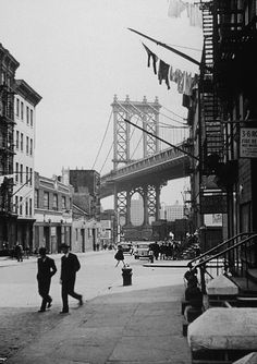 an old black and white photo of people walking down the street in front of a bridge