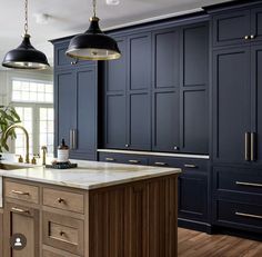 a kitchen with dark blue cabinets and white marble counter tops, two pendant lights hanging over the island