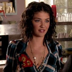 a woman with curly hair wearing a checkered shirt and gold necklace in a kitchen