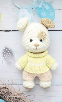 a crocheted teddy bear wearing a yellow sweater and pants sitting on a white wooden surface