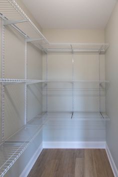 an empty walk in closet with white shelving and wood flooring on the side