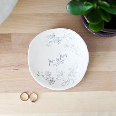 two wedding rings sitting on top of a white plate next to a potted plant