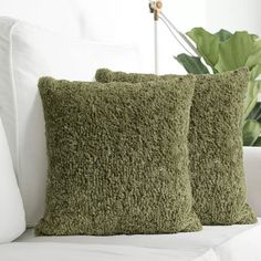 two green pillows sitting on top of a white couch next to a potted plant