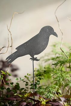 a metal bird sitting on top of a wooden stake in front of some leaves and plants