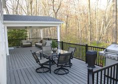 a deck with chairs, table and grill on top of it in front of trees